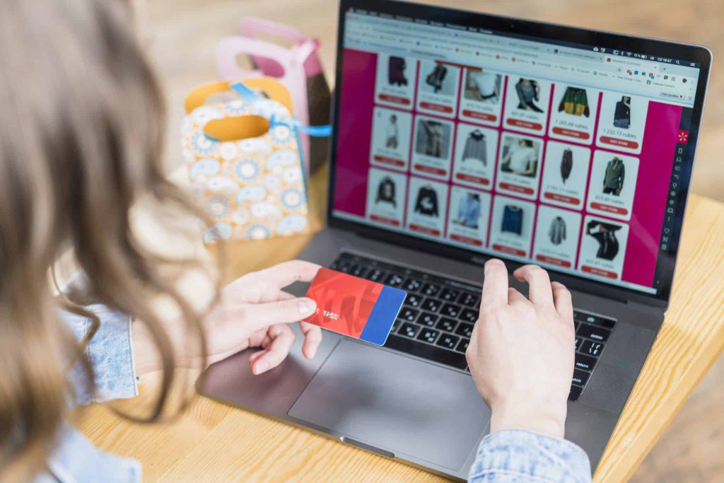 woman-holding-credit-card-front-laptop-with-shopping-website Femme qui tient sa carte de crédit pour commander un article sur un site internet de vêtements